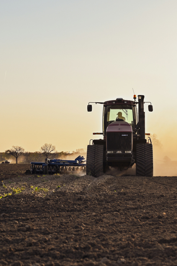 KI generiert: Ein Traktor pflügt bei Sonnenuntergang über ein offenes Feld.
