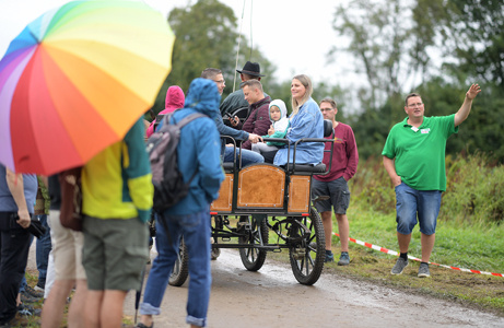 Eine Gruppe Menschen mit Regenschirmen, darunter ein bunter Schirm, hört einem Sprecher neben einer Kutsche zu.