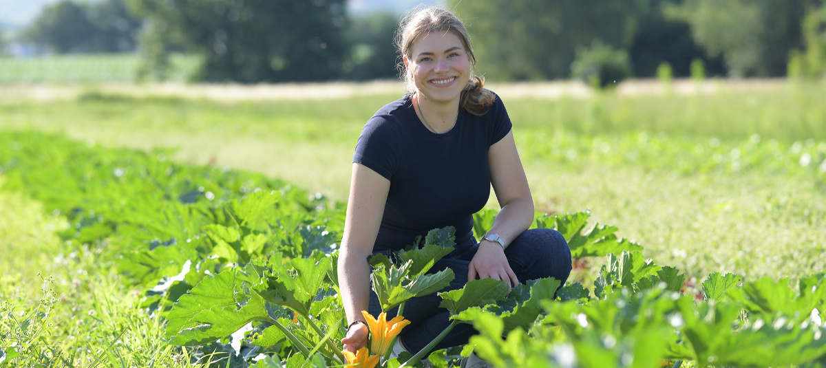 Zwei Mitarbeiterinnen in grünem T-Shirt in einem Bioladen. Die vordere Frau hält eine Packung Weizenmehl in der Hand, im Hintergrund steht die zweite Frau mit einem Einkauf voller Lebensmittel.