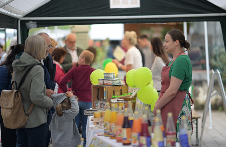 Eine Gruppe von Menschen versammelt sich um einen Essensstand auf einem Freiluftmarkt, Ballons sind sichtbar.