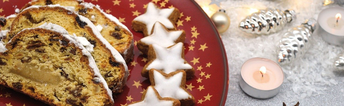 Ein Teller mit weihnachtlichem Stollen und sternförmigen Plätzchen, daneben Kerzen und silberne Dekoration.