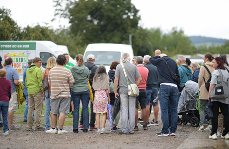 Gruppe von Menschen versammelt sich im Freien, einige stehen vor einem weißem Transporter.