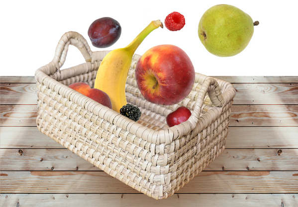 Geflochtener Korb mit frischem Obst, darunter Bananen, Äpfel, Birne, Zitrone und Trauben. Der Korb steht auf einem Holztisch.