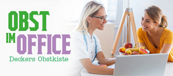 Zwei Frauen sitzen gemeinsam vor einem Laptop in einem Büro. Eine Frau in weißem Oberteil erklärt etwas, die andere in einem orangen Shirt hört zu. Im Vordergrund steht ein Obstkorb mit Äpfeln und Bananen.