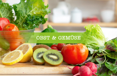 Zwei Frauen sitzen an einem Tisch, eine davon mit Laptop, und sprechen miteinander, daneben eine Schale mit Obst. Darüber liegt ein grünes Banner mit der Aufschrift 'BÜROKISTEN'.