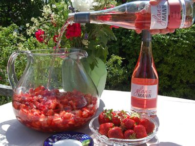 Wein und Erdbeeren auf einem Tisch im Freien, daneben Gläser und Flasche Roséwein.