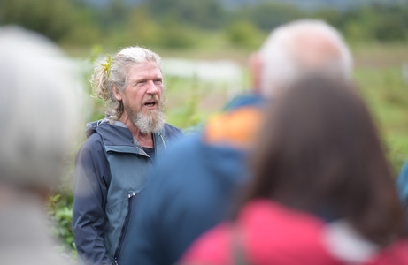 Ein älterer Mann spricht im Freien vor einer kleinen Gruppe.