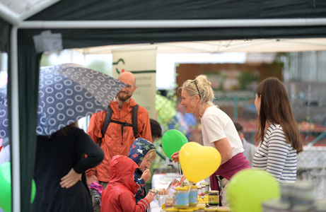 Kinder und Erwachsene stehen an einem Stand mit bunten Luftballons – fröhliche Atmosphäre trotz Regen, evtl. ein Bastel- oder Infostand.