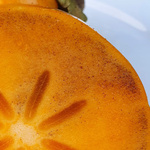 Ein runder Ausschnitt, der einen Querschnitt einer Kaki-Frucht zeigt, deren oranges Fruchtfleisch feine braune Sprenkel aufweist, mit der Unterschrift 'Braune Flecken in der Kaki'.