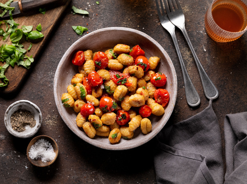Teller mit frisch zubereiteten Gnocchi, dazu Kräuter und Olivenöl auf einem Tisch.