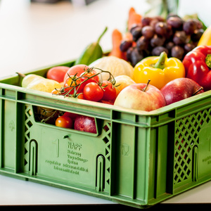 Eine grüne Gemüsekiste gefüllt mit frischem Obst und Gemüse wie Tomaten, Äpfeln und Paprika – ideal für Bürobelieferung.