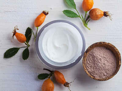 Frische Sanddornfrüchte und ein Glas Joghurt auf hellem Untergrund.