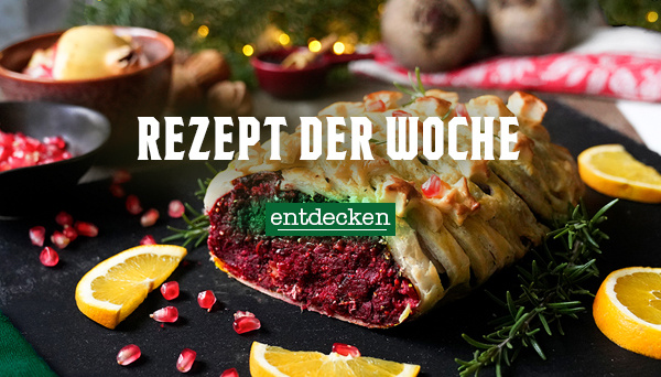 Nahaufnahme einer cremigen Suppe, garniert mit Kräutern und Pilzen, in einer Schüssel. Im Hintergrund liegen Zwiebeln. Text im Bild: „Rezept der Woche – entdecken