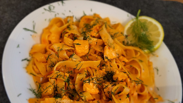 Ein Teller mit spiralförmig geschnittenen Karottenstreifen, serviert wie Pasta. Garniert mit frischen Kräutern und einer halben Limette. Die Farben wirken frisch und sommerlich.