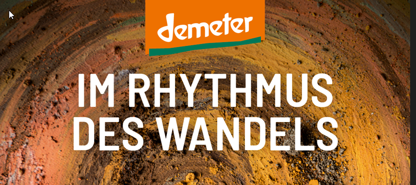 Das Demeter-Logo steht über dem weißen Text „Im Rhythmus des Wandels“, der auf einem farbenfrohen, erdigen Hintergrund mit kreisförmigen Pinselstrukturen in Braun-, Orange- und Gelbtönen geschrieben ist.