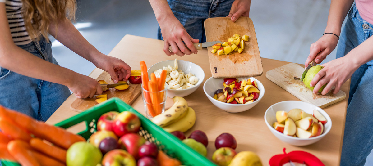 Acht Kinder genießen draußen nach der Schule einen gesunden Snack. Im Vordergrund erkennt man viele Schultaschen.