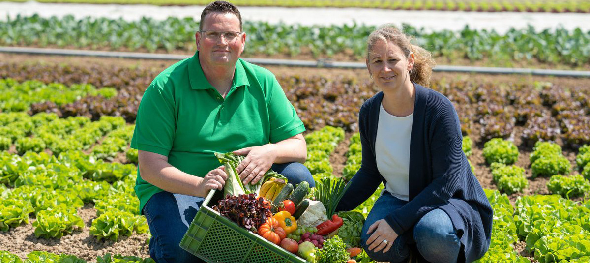 Christoph Decker uns Leonie Schittenhelm auf dem Acker mit einer Grünen Kiste voller Obst und Gemüse